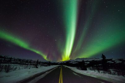 green aurora over a highway with snow to the sides
