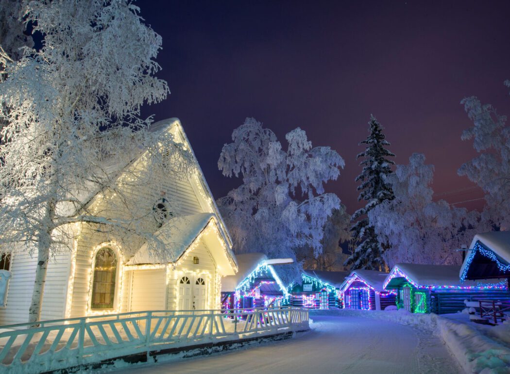snow-covered early 20th century hourses decorated in Christmas lights in a historic park