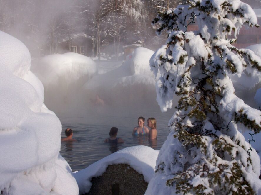 people relax at a natural hot springs pool surrounded by snow covered rocks