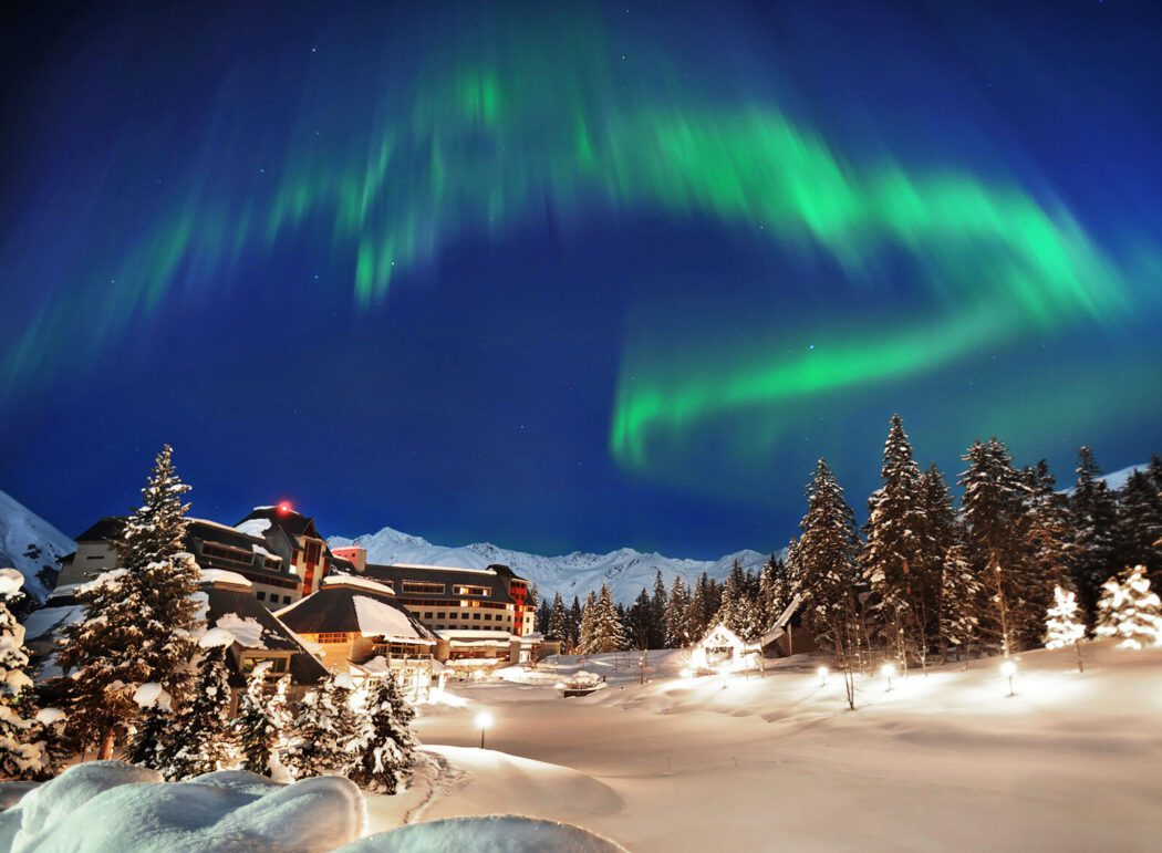 green aurora over a resort surrounded by snow and spruce trees