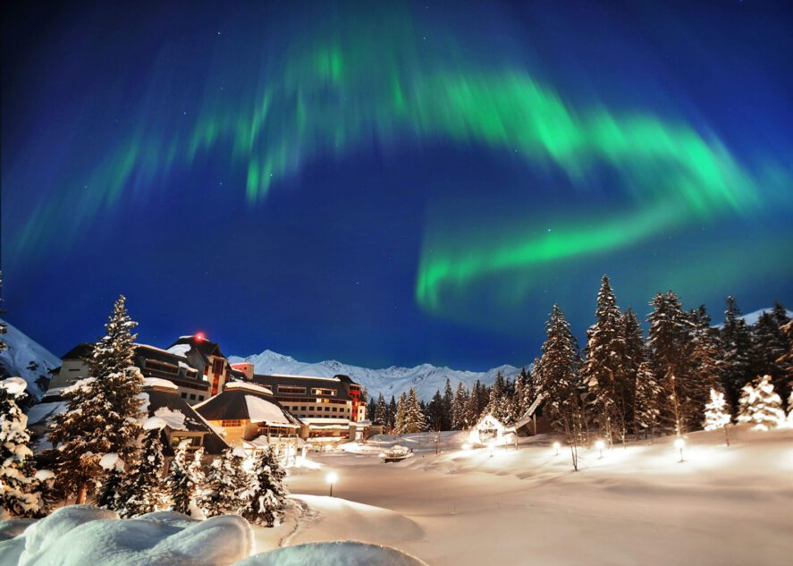 green aurora over a resort surrounded by snow and spruce trees