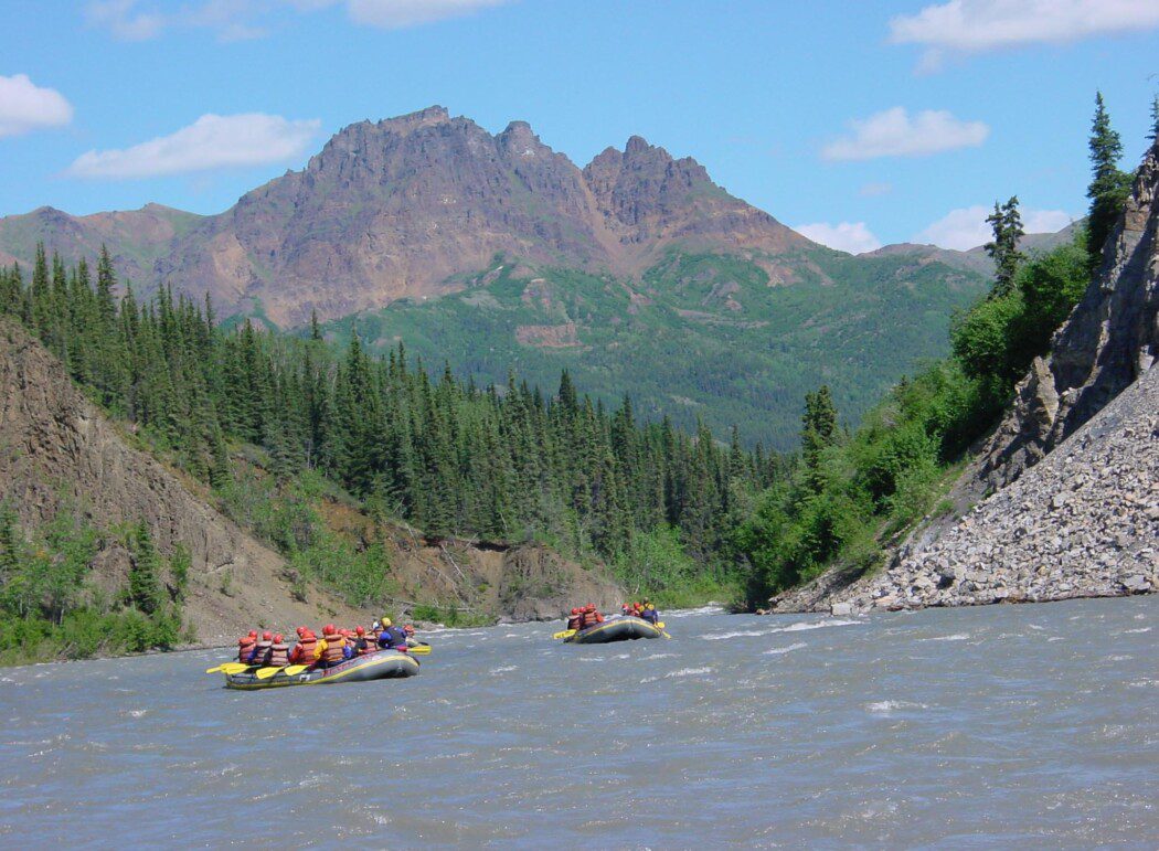 two river rafts with people exploring a river surrounded by a mountainous landscape