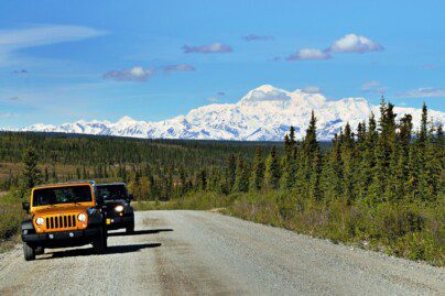 two Jeeps on a remote highway, with Denali and spruce trees in the background