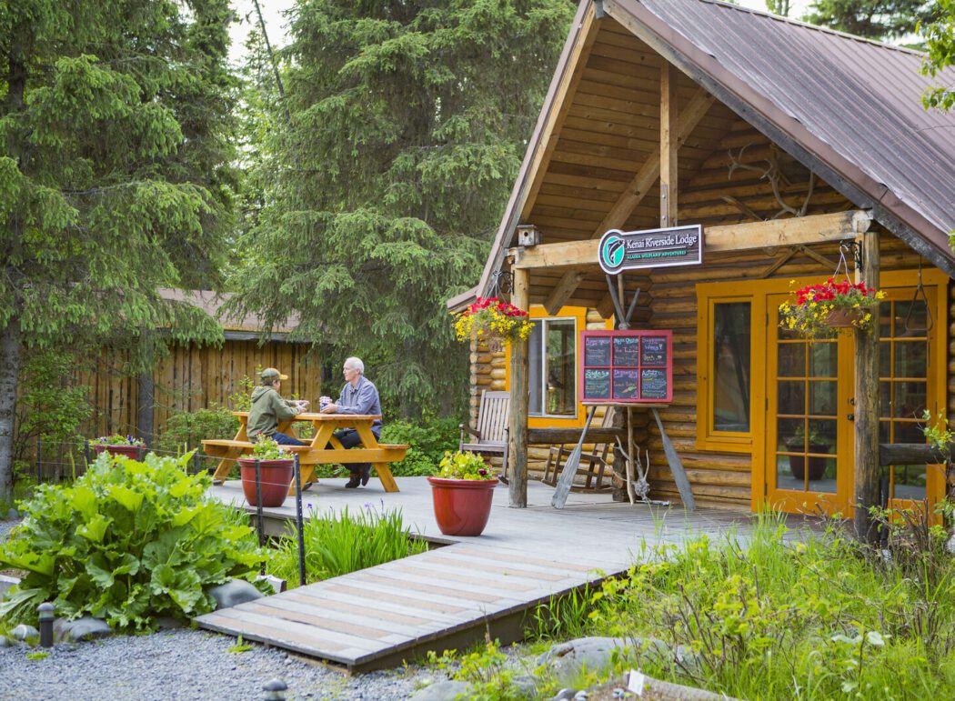 two people sitting at a picnic bench in front of a remote wilderness lodge in Alaska