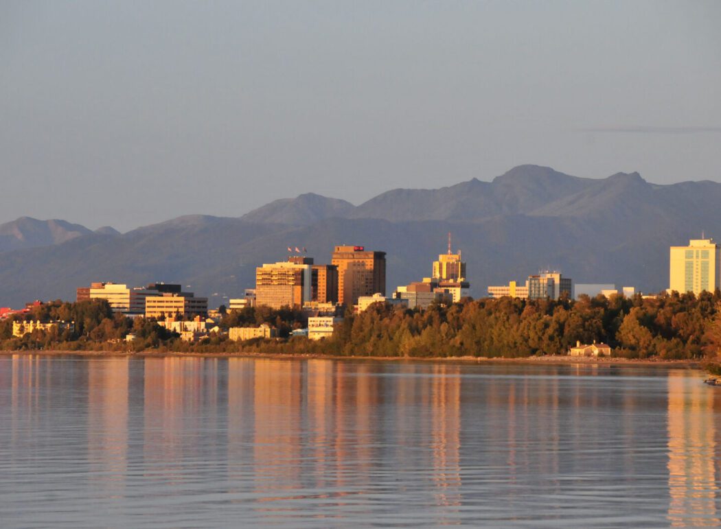 the city skyline of Anchorage, Alaska with water in the foreground and mountains in the background
