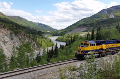 a passenger train passes along a river through a forested valley