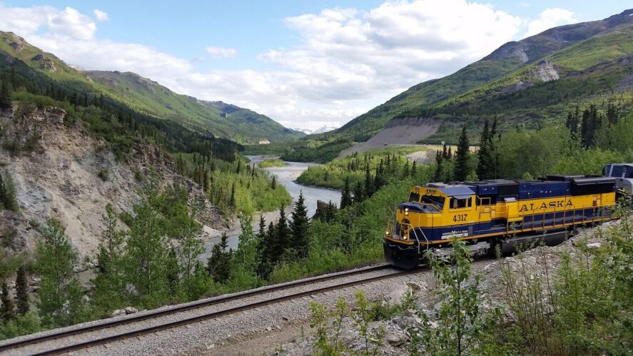 a passenger train passes along a river through a forested valley