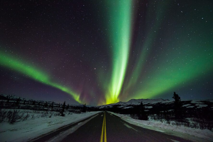 Green aurora over a winter landscape and highway in Alaska