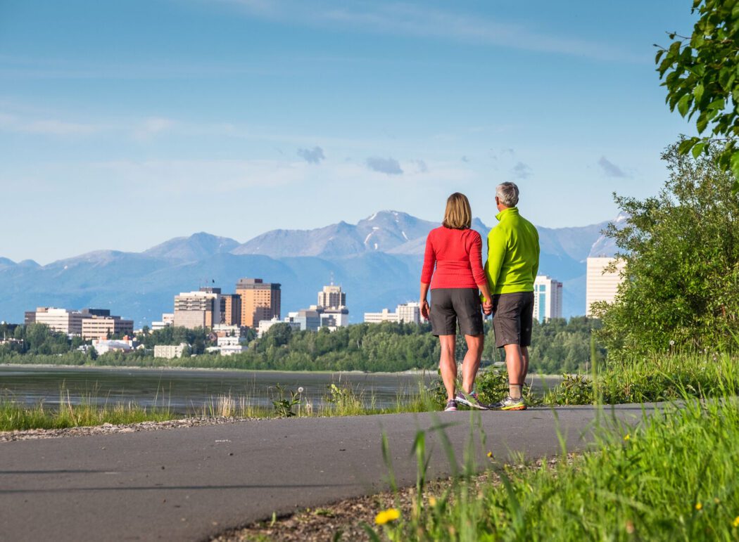a couple holding hands on a paved path looking out to the skyline of Anchorage, Alaska