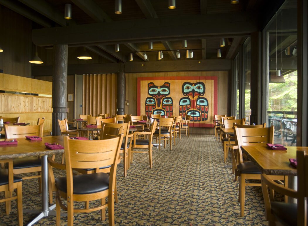 wooden tables and chairs and Alaska Native art on the wall of a dining room in an Alaskan lodge