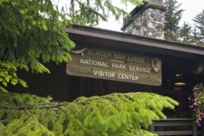 Evergreen trees and a wooden sign on a lodge reading "Glacier Bay Lodge | National Park Service Visitor Center"