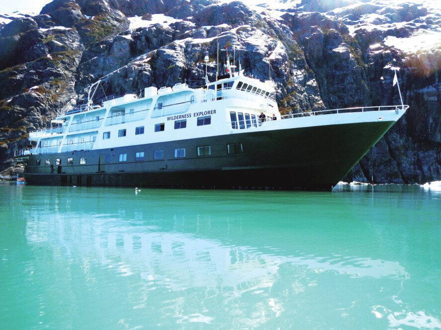 the small cruise ship "Wilderness Explorer" in calm water by a rocky shore