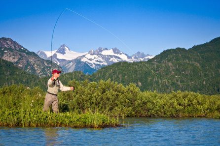 a man fly-fishing in a lake surrounded by vegetation and mountains