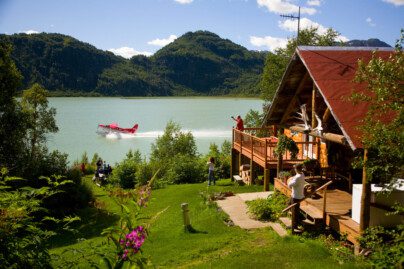 People at a log-cabin lodge watching a float-plane take off from an adjacent lake