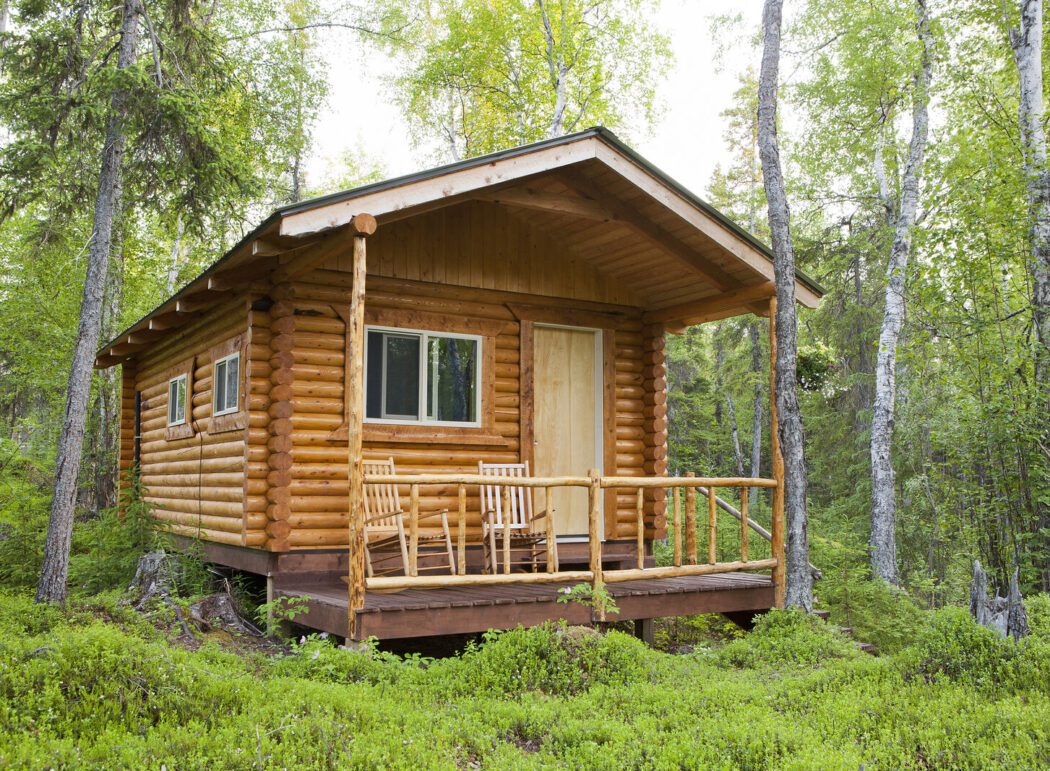 a log cabin with wooden chairs on a porch in a remote Alaskan forest