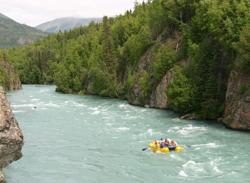 People in a yellow river raft on the turquoise waters of the Kenai River