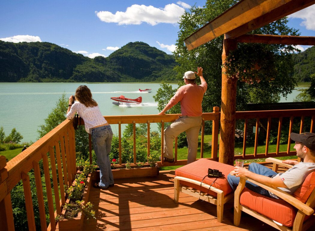 three people on the deck of a log-cabin lodge overlooking a lake