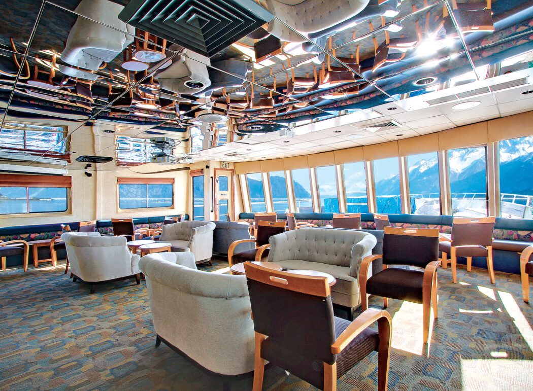 a lounge area on a cruise ship with comfy chairs and window views to the bow