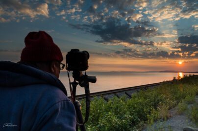 a person looking through a camera on a tripod at a summertime sunset in Alaska