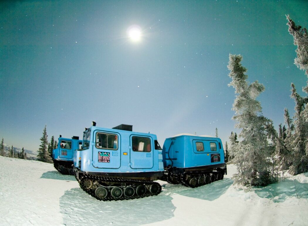 A blue snowcoach in a snowy boreal forest at night