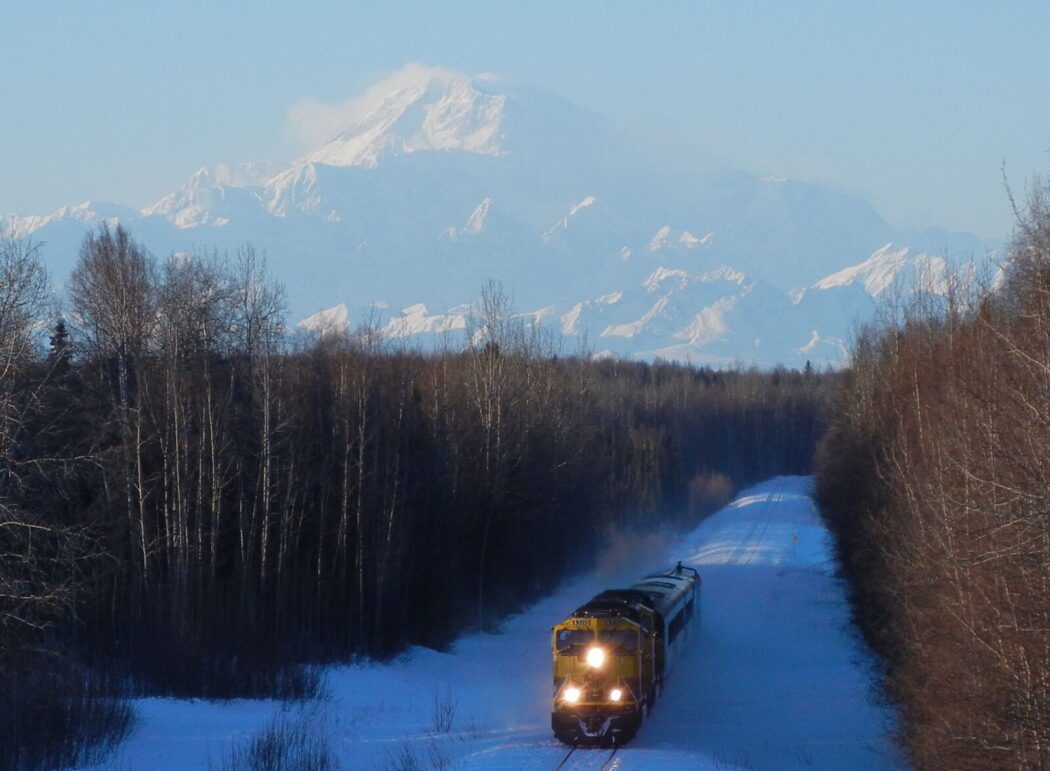 the Alaska Railroad train in the foreground traveling through a winter forest; Denali mountain in background