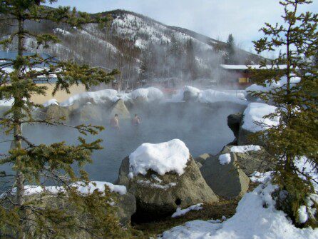 people relaxing in a natural hot spring lake surrounded by snow-capped rocks