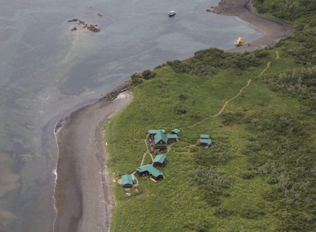 an aerial view of a coastline, a lodge, and a float plane