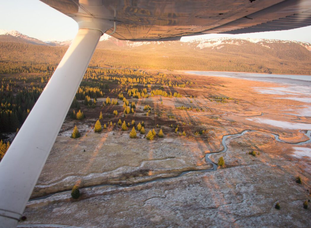 Orange and yellow sunlight illuminates Gustavus, Alaska from a seaplane window.