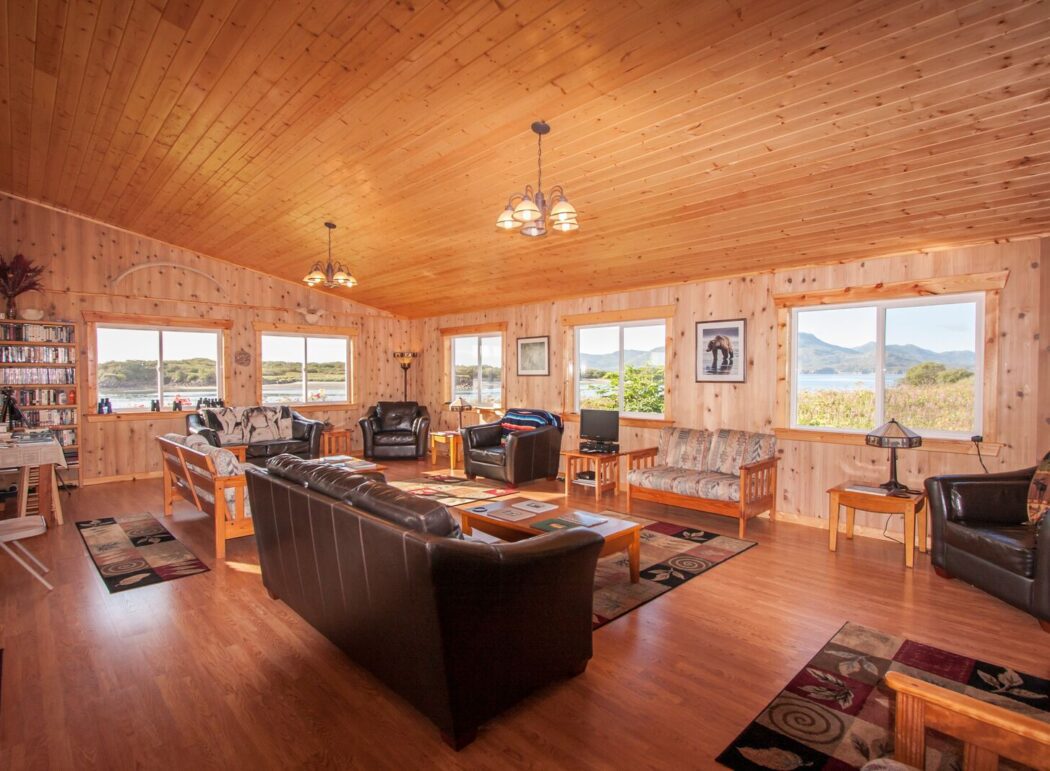 wood-paneled common area of a lodge, featuring cozy furniture, book cases and window views