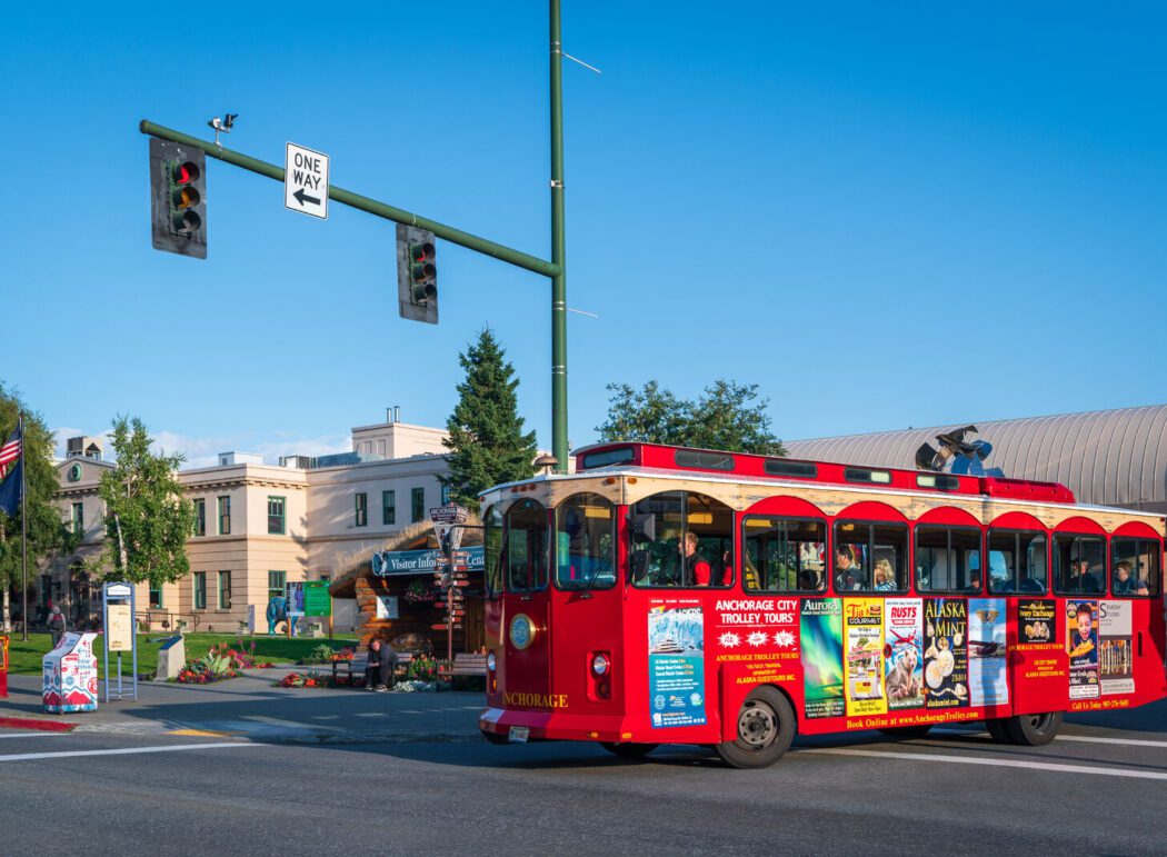 A red trolley bus with tourists driving through downtown Anchorage, Alaska