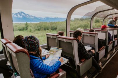 people on a train looking at Alaskan scenery through dome-car windows; one woman holds a map of Alaska