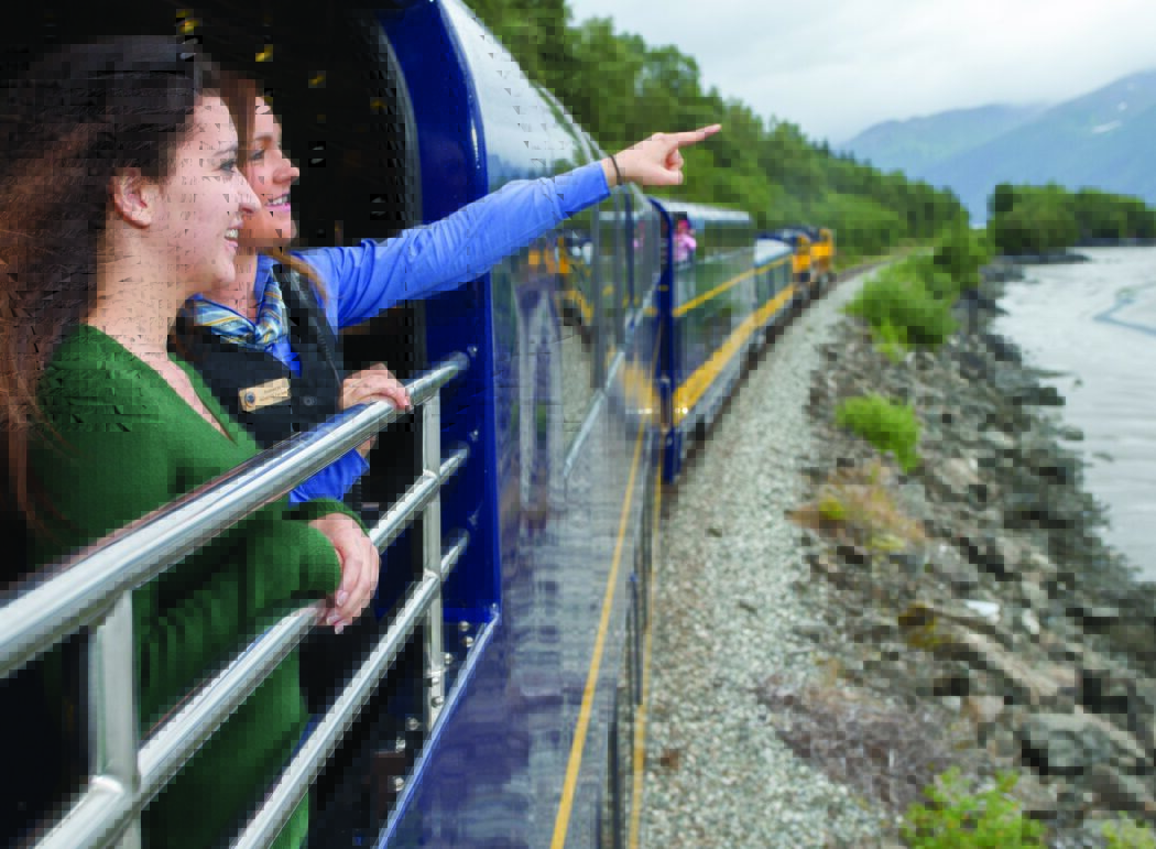 two women, one pointing, on the viewing platform of an Alaska Railroad train