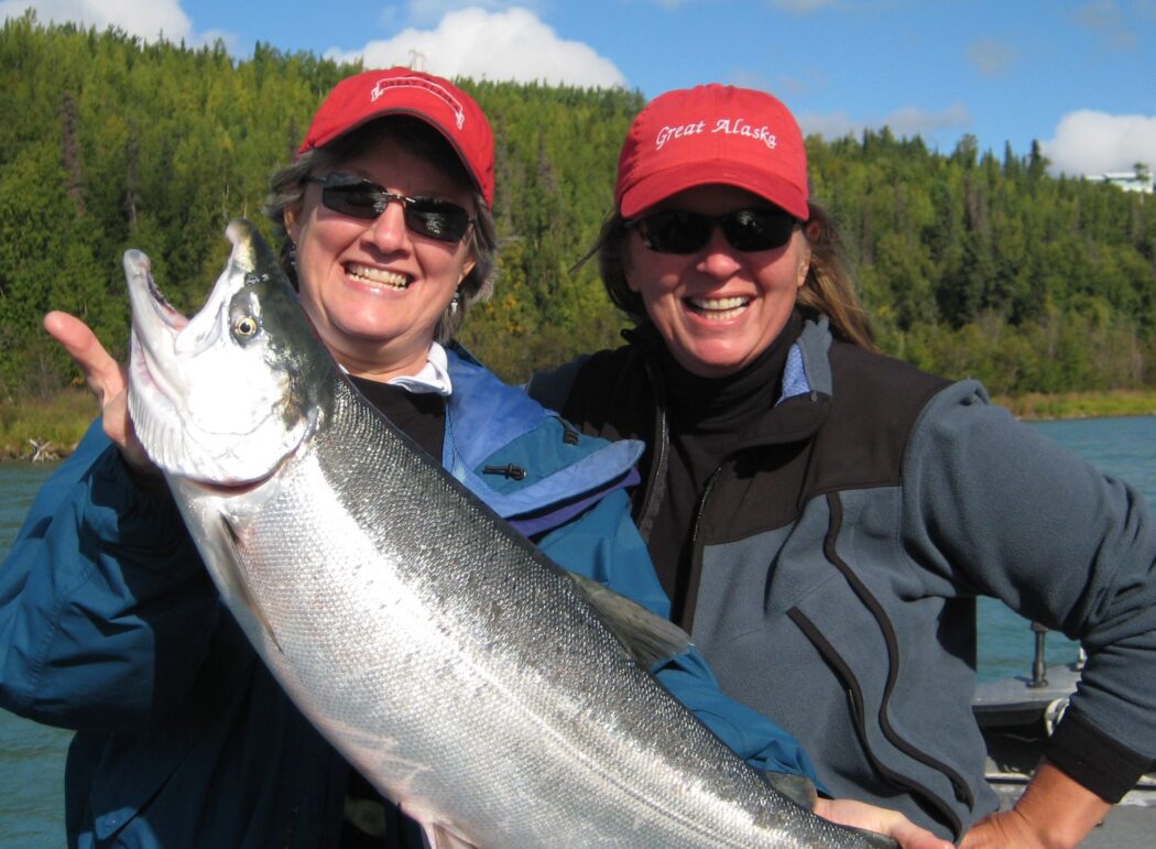 two women in on a boat in a river holding a salmon