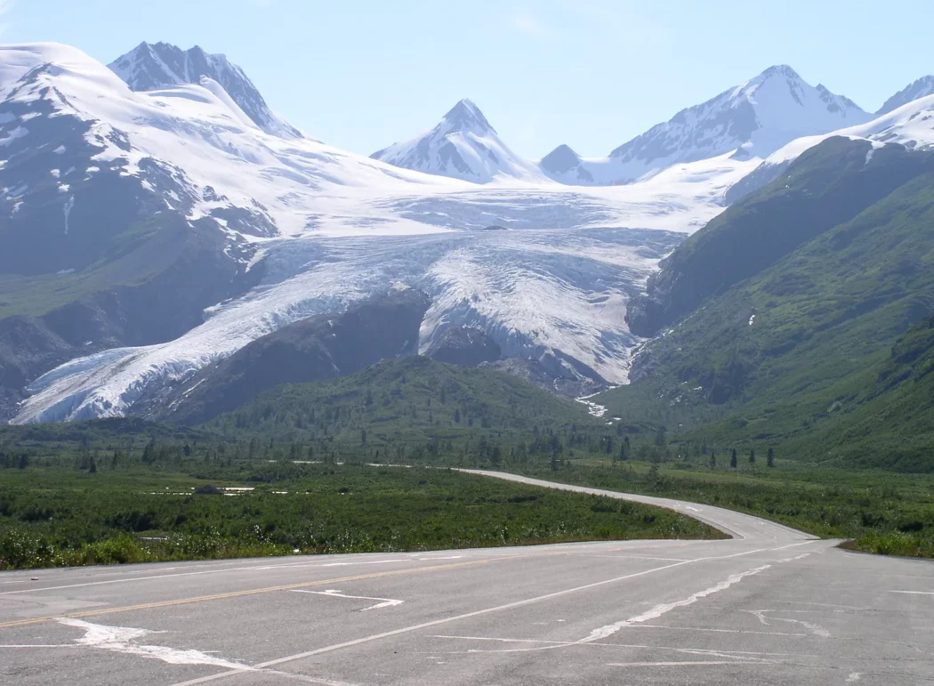 an alpine glacier in front of a paved highway through a mountain pass