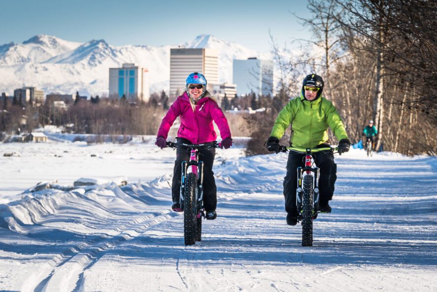 two people in winter gear fat tire biking on a snow covered trail outside downtown Anchorage, Alaska