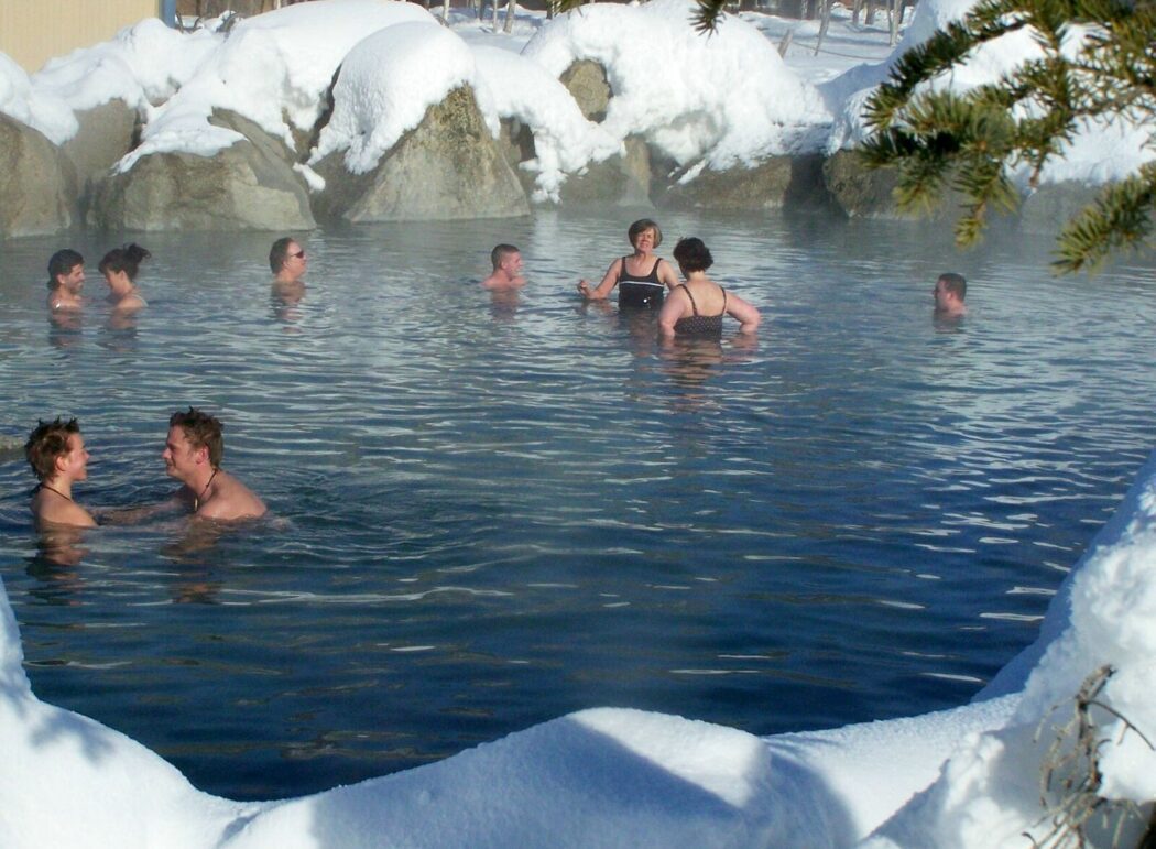 people relaxing in a hot springs pool circled by snow-covered rocks