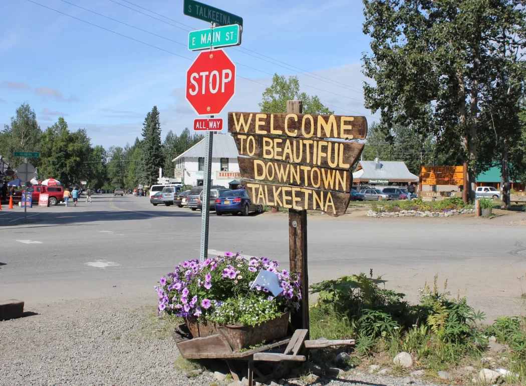 a stop sign at the intersection of Talkeetna St and Main St and a wooden sign reading "Welcome to Beautiful Downtown Talkeetna"