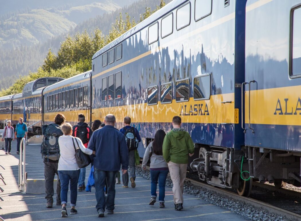 people standing outside the blue and yellow "Alaska Train" at a train station in Seward, Alaska