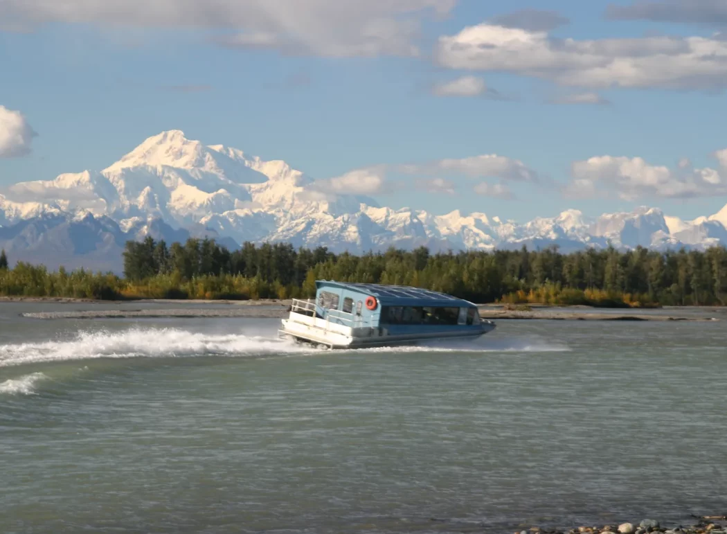 a jet boat speeds on a river with the Alaska Range mountains in the background