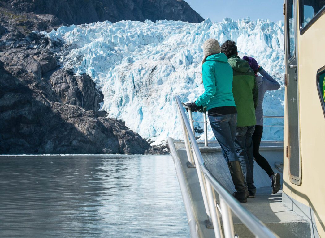 two people on the deck of a tour boat looking at a tidewater glacier