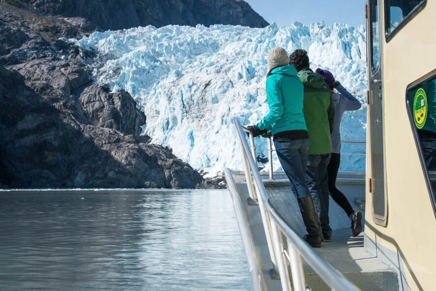 two people on the deck of a tour boat looking at a tidewater glacier
