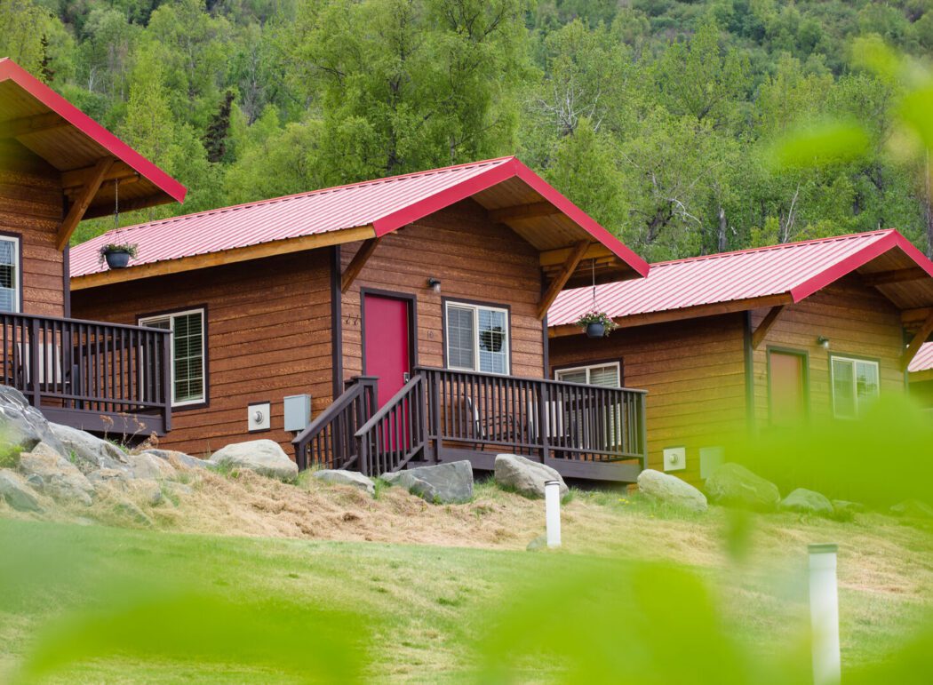 three cabins with red roofs and red doors; forest in background