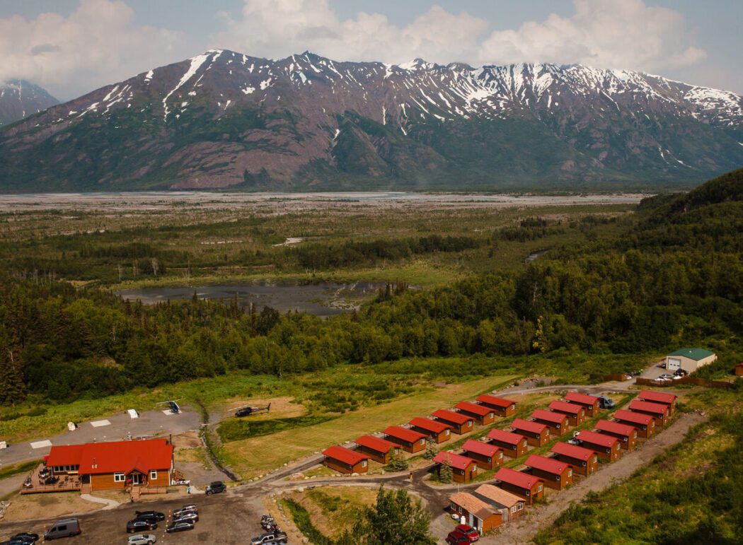 rows of red roofed cabins and a larger lodge overlooking a valley and mountains