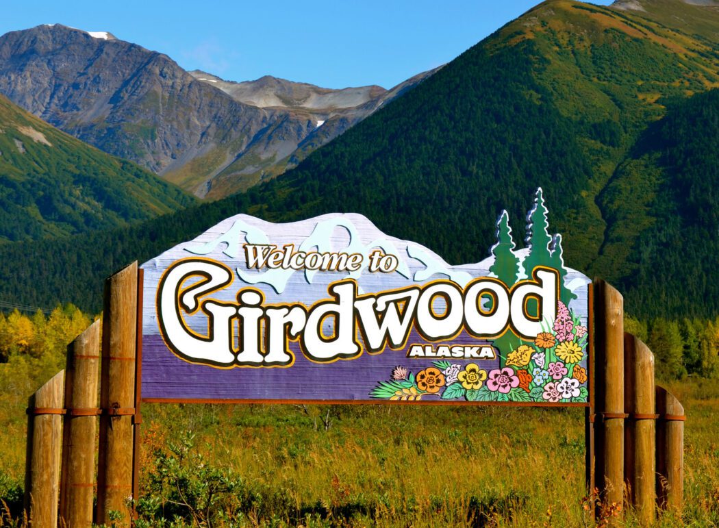 a wooden sign reading "Welcome to Girdwood, Alaska" in front of mountains and clear blue sky