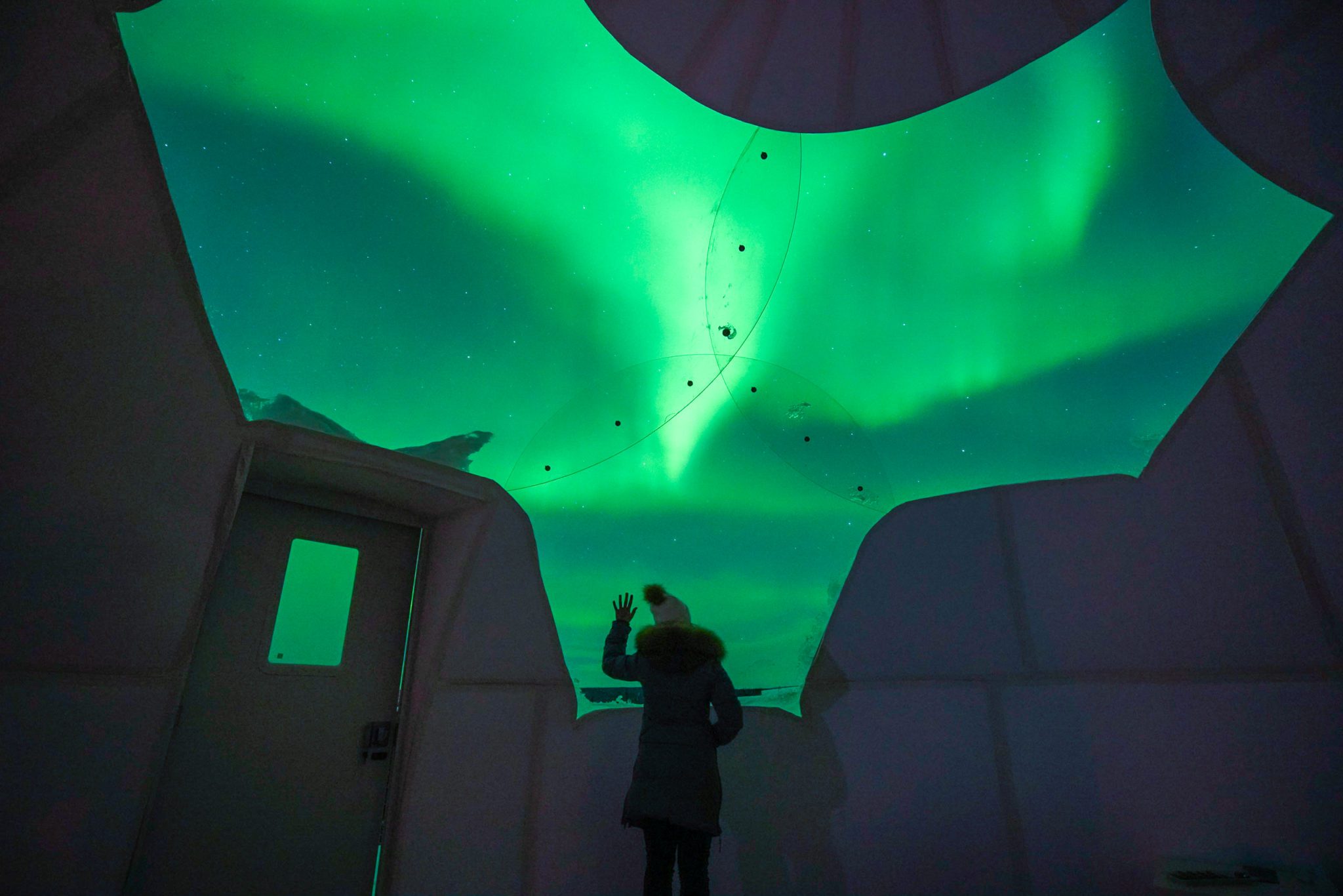 a person viewing green aurora through a fiberglass dome
