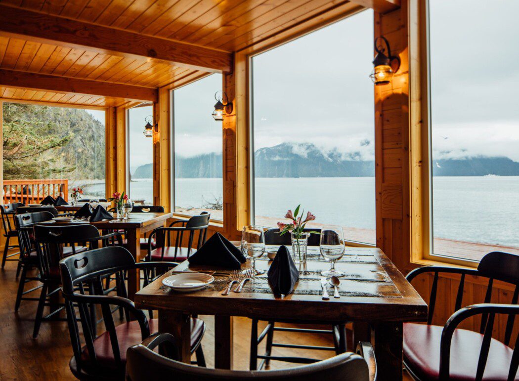 neatly set dining tables in a wooden patio with window views of Resurrection Bay