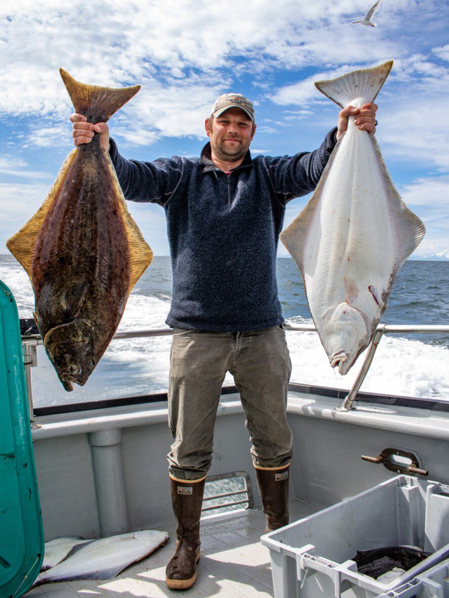 a man on a fishing charter boat holds up two halibut