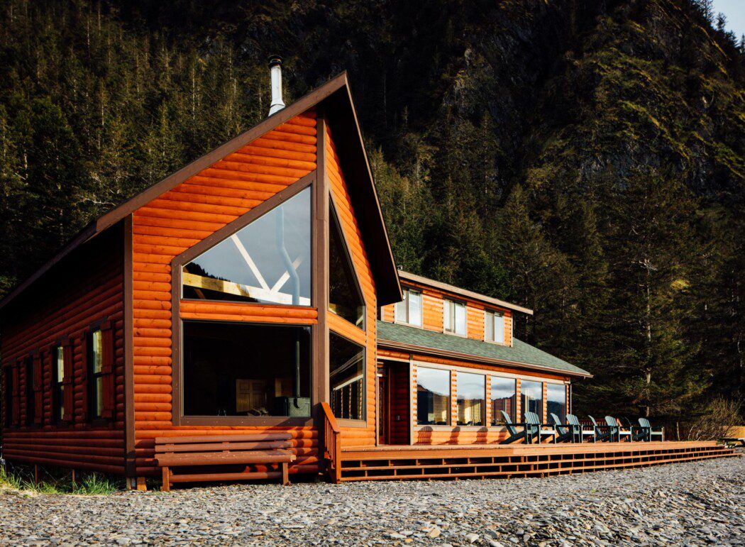 a log cabin lodge with chairs on a deck and steep mountain cliffs behind