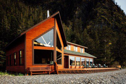 a log cabin lodge with chairs on a deck and steep mountain cliffs behind