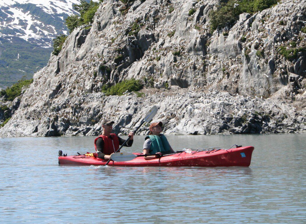 two people in a tandem kayak along a rocky coast
